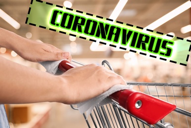 Image of Woman holding shopping cart handle with tissue paper at supermarket, closeup. Preventive measure in public places during coronavirus outbreak