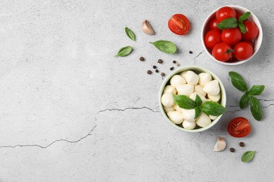 Photo of Delicious mozzarella balls in bowl, tomatoes and basil leaves on light gray textured table, flat lay. Space for text