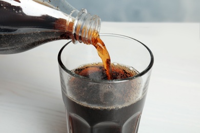 Pouring refreshing soda drink into glass on table, closeup