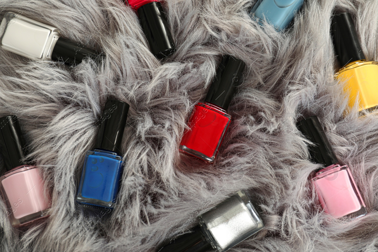 Photo of Bright nail polishes in bottles on grey faux fur, top view