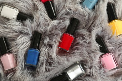 Bright nail polishes in bottles on grey faux fur, top view