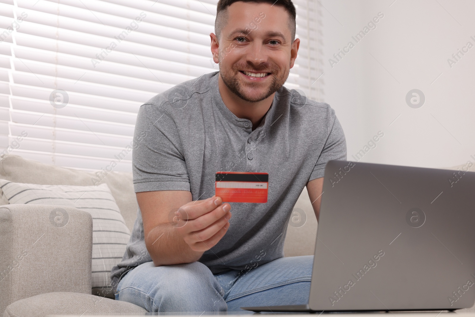 Photo of Handsome man with credit card using laptop for online shopping at home