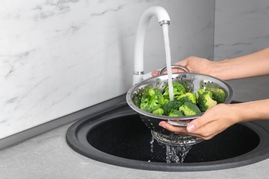 Photo of Woman washing fresh green broccoli in metal colander under tap water, closeup view. Space for text