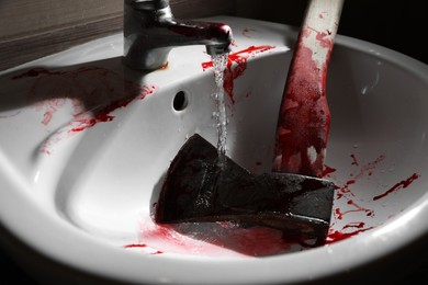 Axe with blood under tap water in sink, closeup