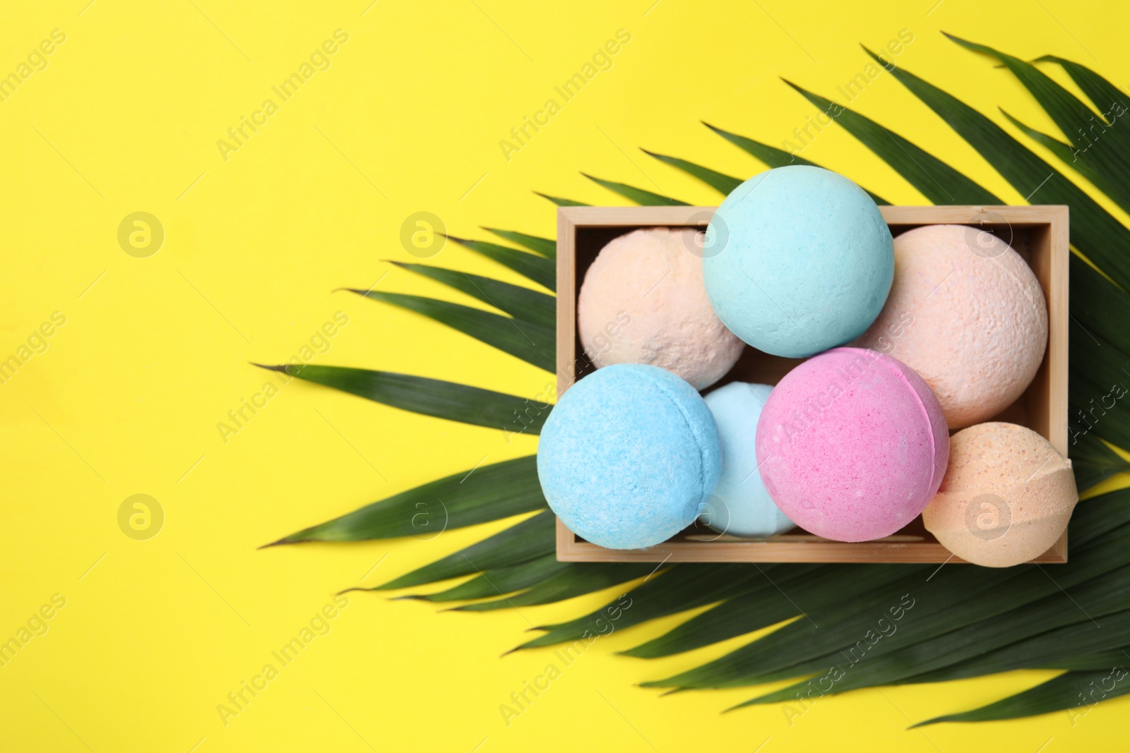 Photo of Wooden crate with bath bombs and green leaf on yellow background, flat lay. Space for text