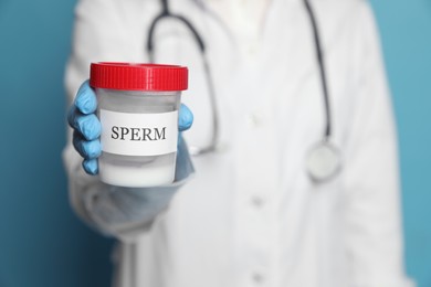 Photo of Doctor holding container with sperm on turquoise background, closeup. Space for text