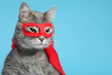 Photo of Adorable cat in red superhero cape and mask on light blue background, space for text