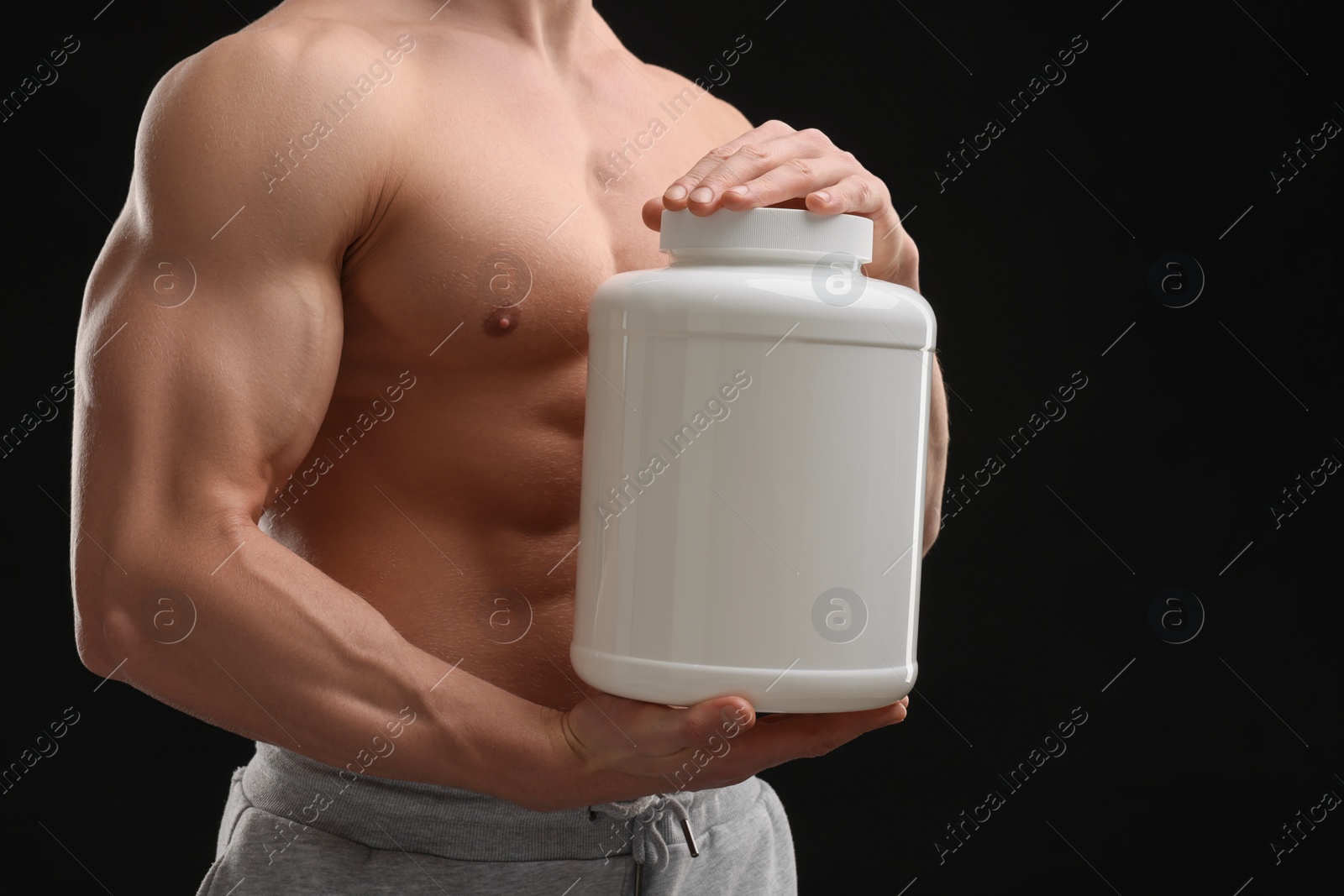 Photo of Young man with muscular body holding jar of protein powder on black background, closeup. Space for text