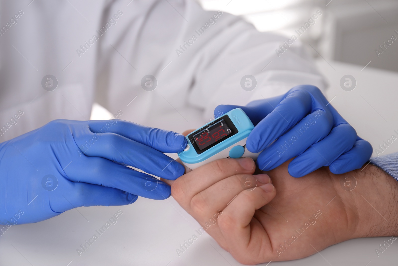 Photo of Doctor checking patient's oxygen level with pulse oximeter at light grey table, closeup