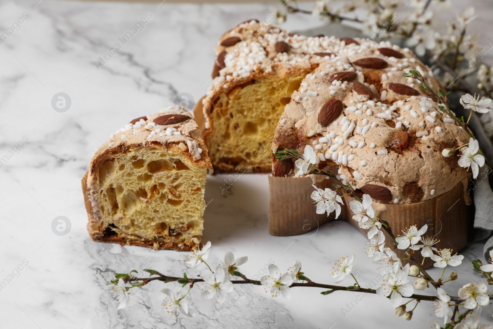 Photo of Delicious Italian Easter dove cake (traditional Colomba di Pasqua) and flowers on white marble table, closeup