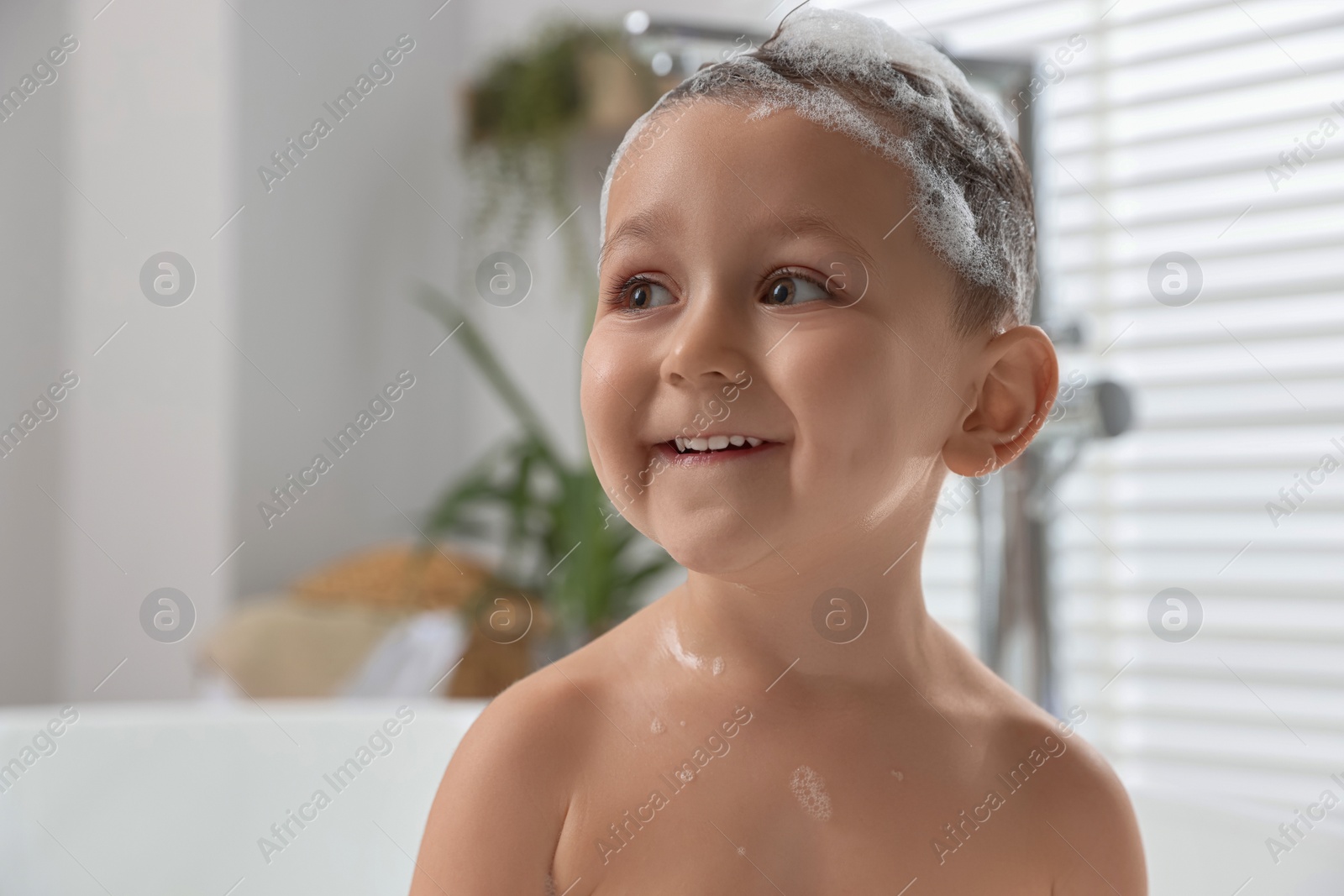 Photo of Cute little boy washing hair with shampoo in bathroom