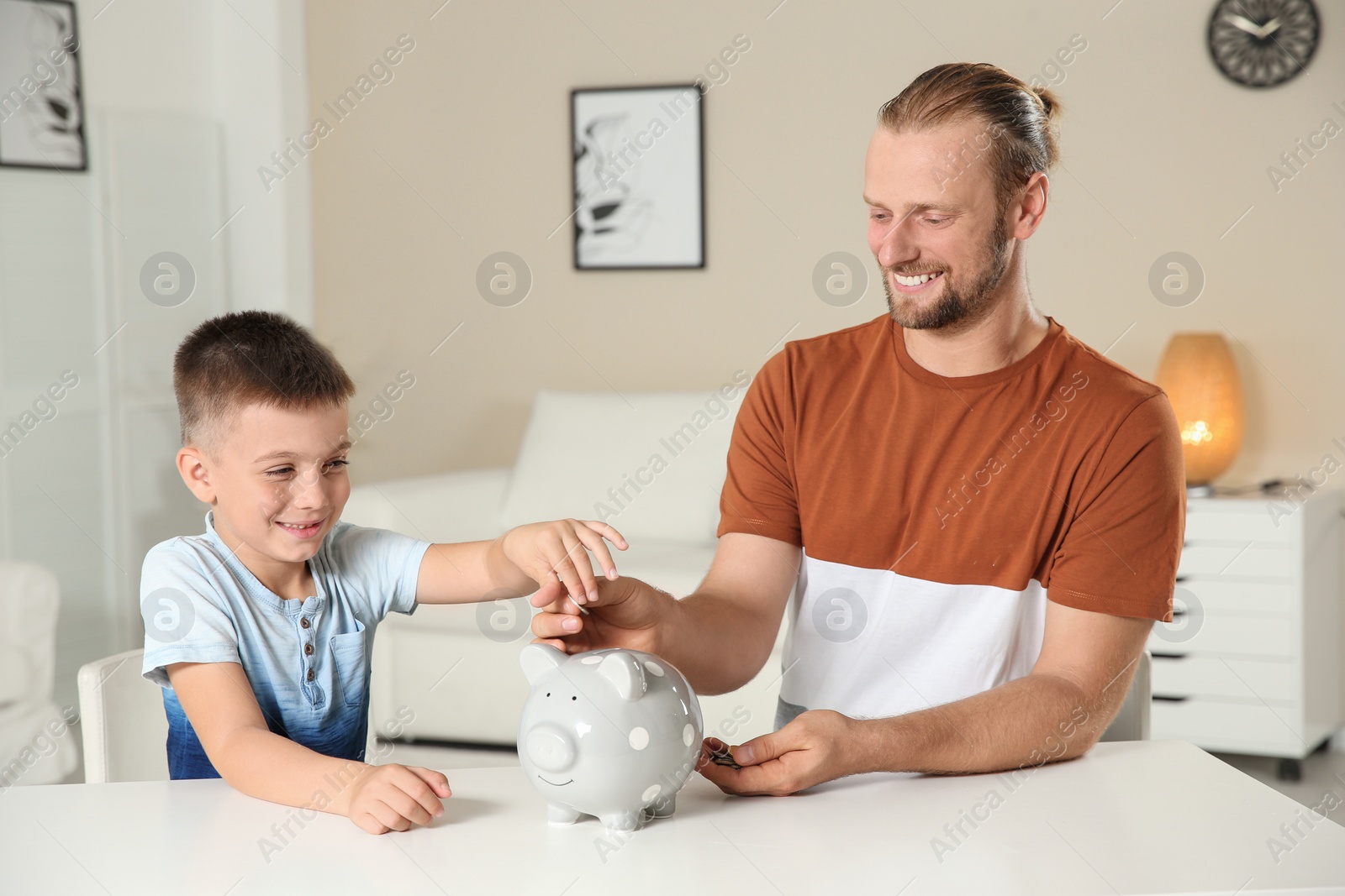 Photo of Father and son putting coin into piggy bank at home