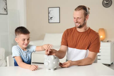 Father and son putting coin into piggy bank at home