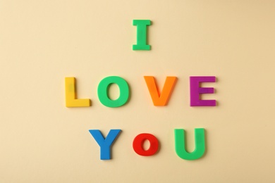Photo of Phrase I LOVE YOU made of plastic letters on beige background, top view