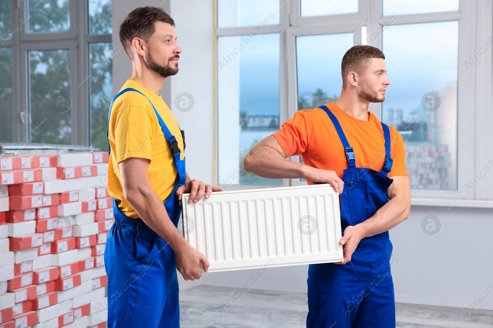 Photo of Professional plumbers with new heating radiator indoors