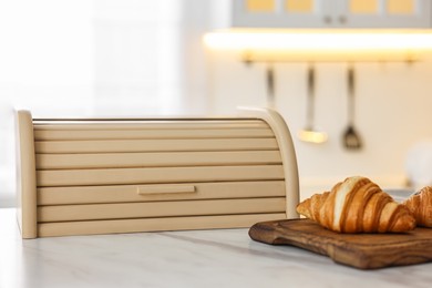 Photo of Wooden bread box and board with croissants on white marble table in kitchen