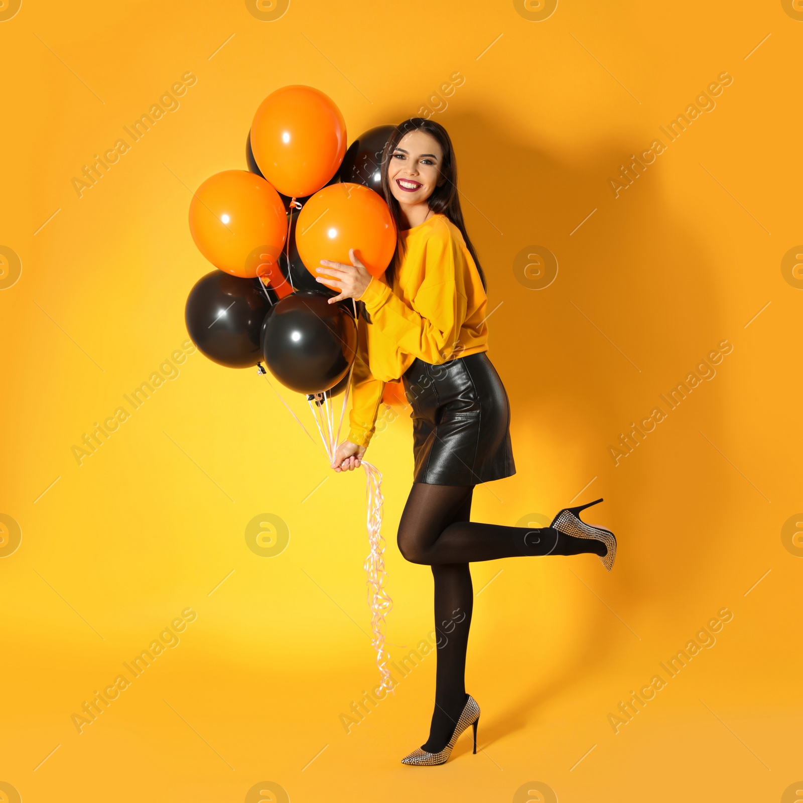 Photo of Beautiful woman with balloons on yellow background. Halloween party