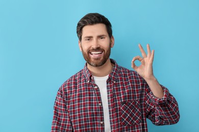 Photo of Portrait of smiling man with healthy clean teeth showing ok gesture on light blue background
