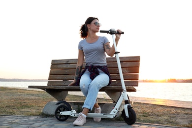 Photo of Young woman with kick scooter sitting on bench outdoors