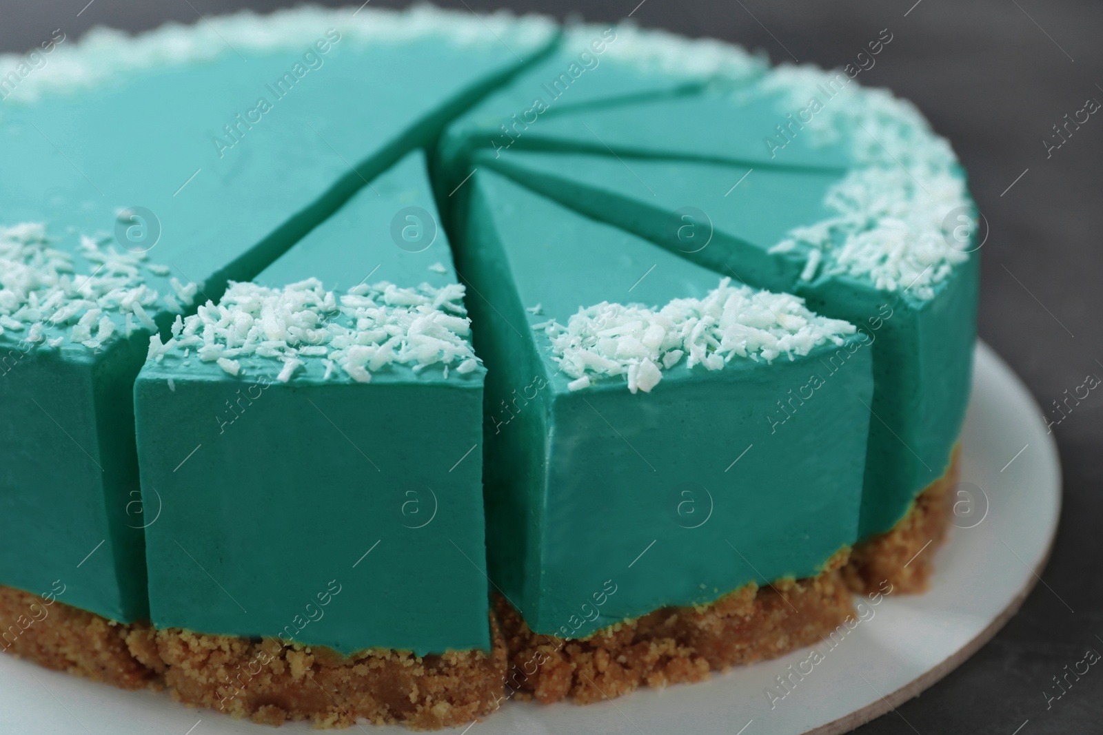 Photo of Sliced tasty spirulina cheesecake on dark grey table, closeup view