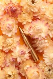 Bullet surrounded by beautiful flowers on orange background, flat lay