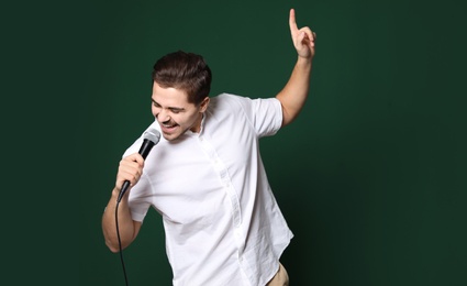 Photo of Young handsome man in casual clothes singing with microphone on color background. Space for text