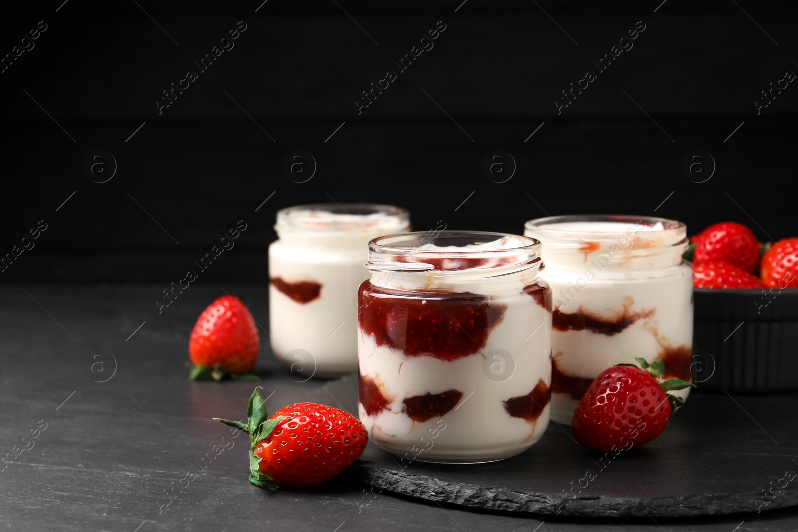 Photo of Tasty yoghurt with jam and strawberries on black table, closeup. Space for text