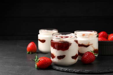 Photo of Tasty yoghurt with jam and strawberries on black table, closeup. Space for text