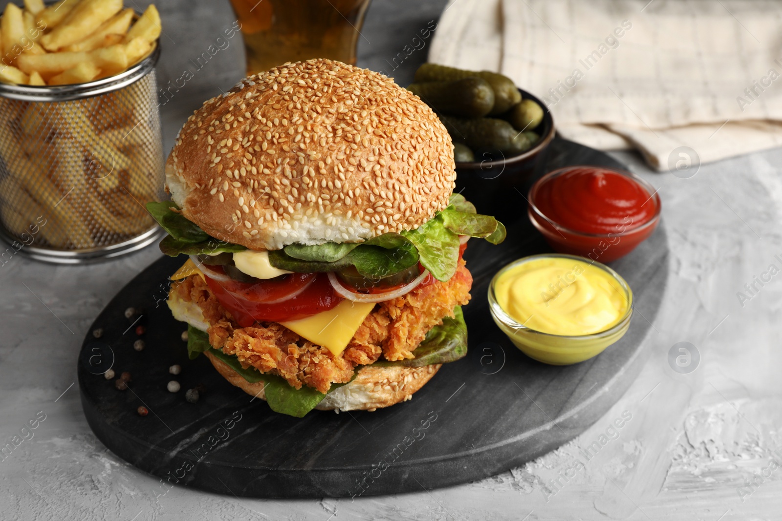 Photo of Delicious burger with crispy chicken patty and sauces on grey table, closeup