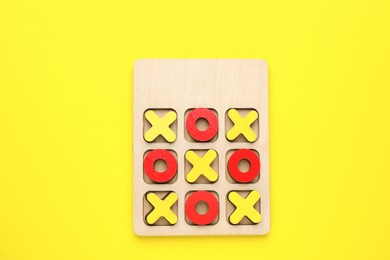 Photo of Wooden tic-tac-toe set on yellow background, top view