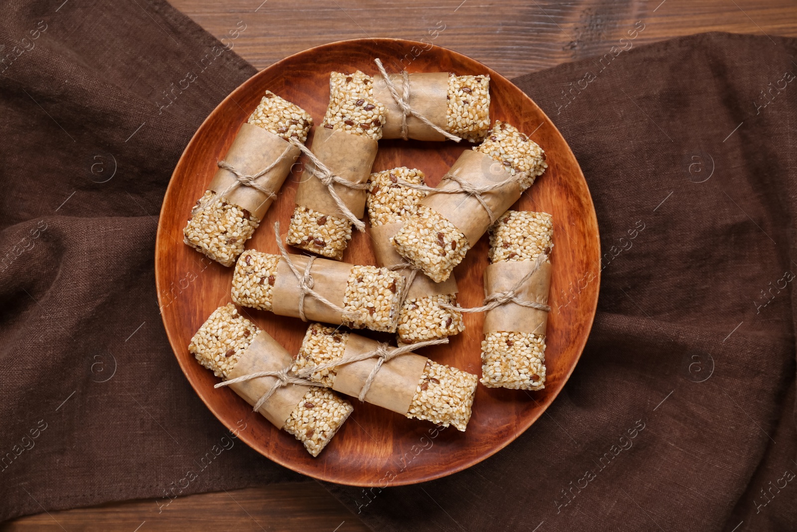 Photo of Plate with tasty sesame seed bars on wooden table, top view