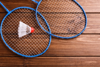 Badminton rackets and shuttlecock on wooden table, flat lay