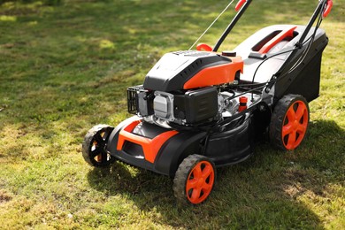 Photo of Modern lawn mower on green grass outdoors