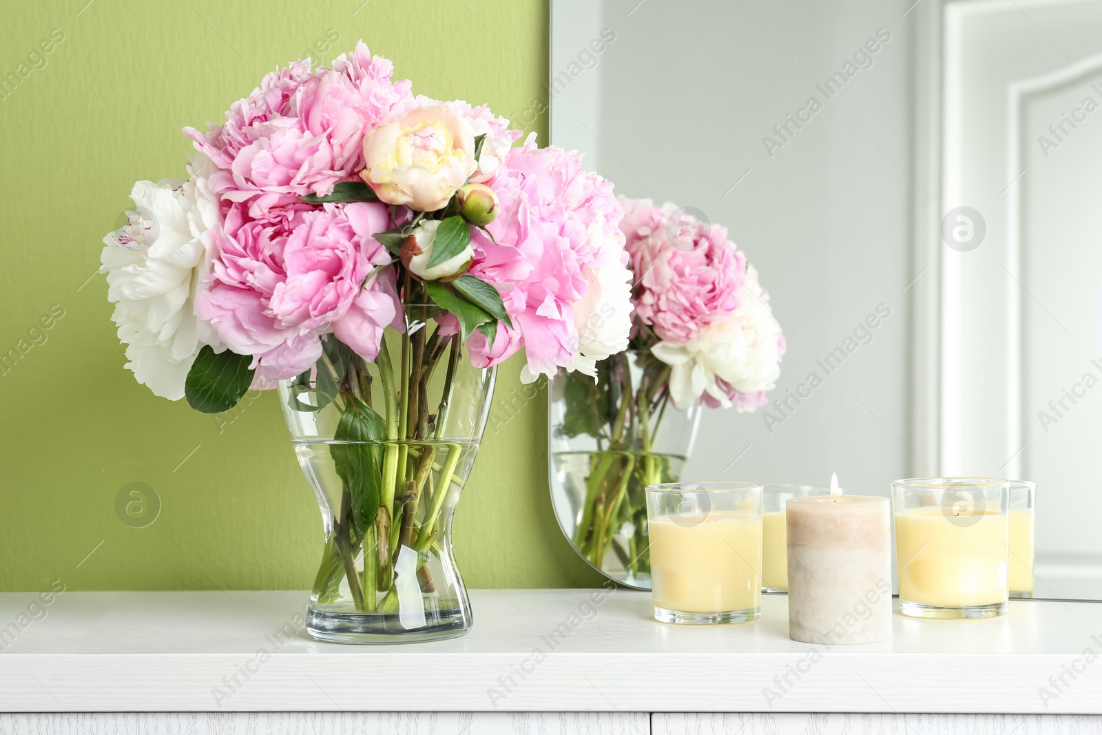 Photo of Beautiful peonies and candles on white dressing table near green wall