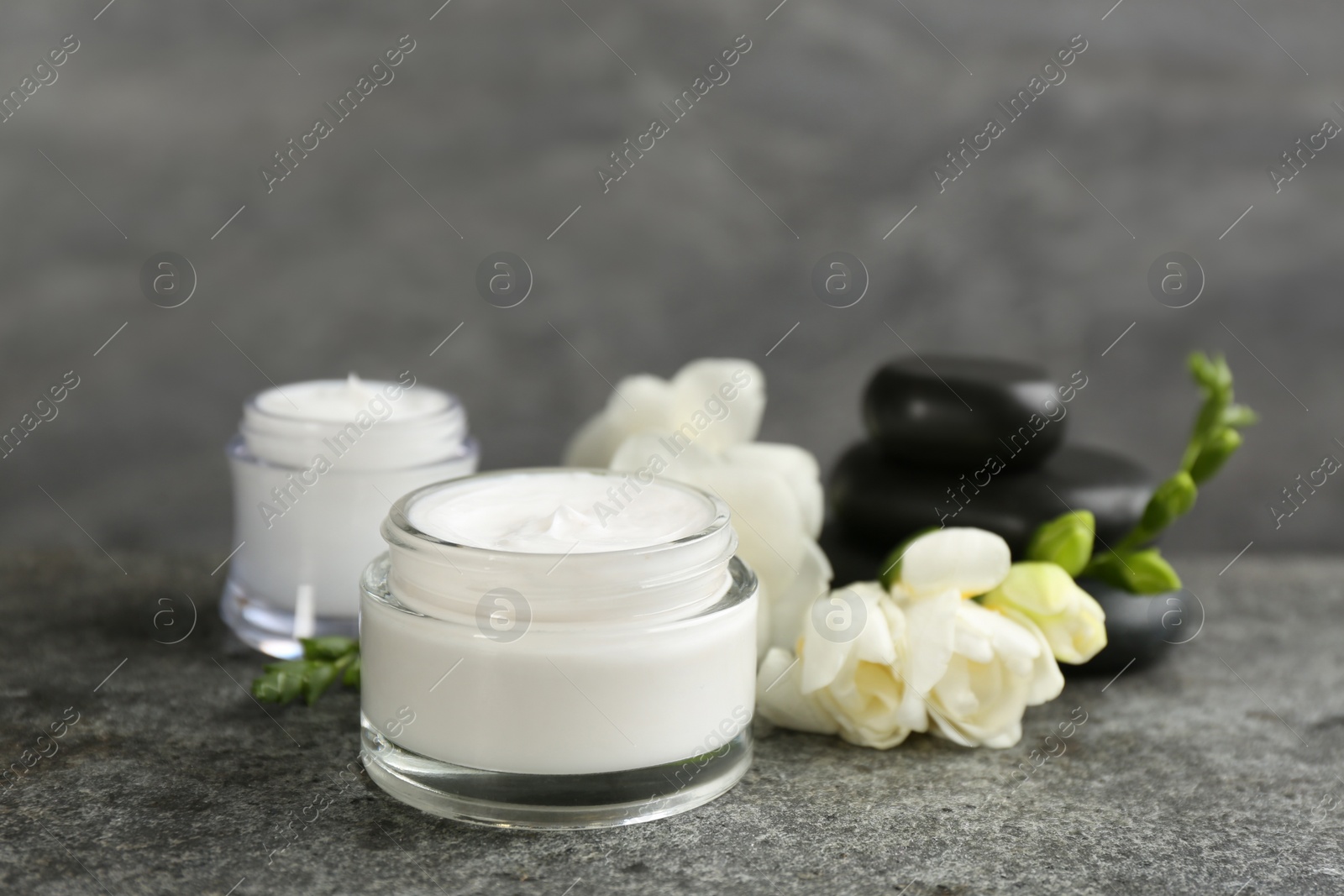 Photo of Beautiful spa composition with cosmetic products, stones and flowers on grey table