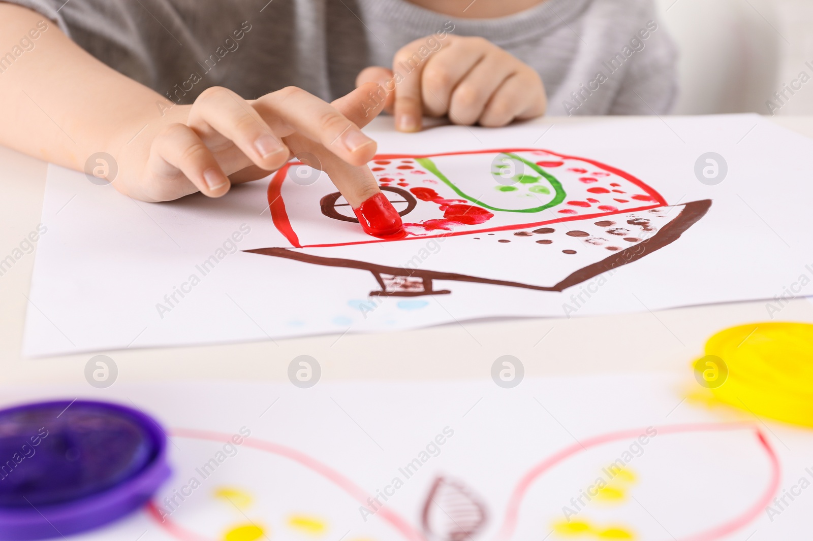 Photo of Little boy painting with finger at white table indoors, closeup