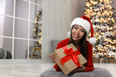 Photo of Happy young woman in Santa hat with Christmas gift at home