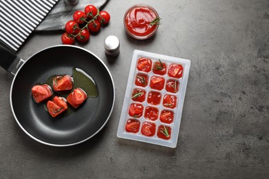 Flat lay composition of melting ice cubes with tomatoes, oil and rosemary on grey table
