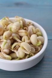 Photo of Sprouted kidney beans in bowl on light blue wooden table, closeup