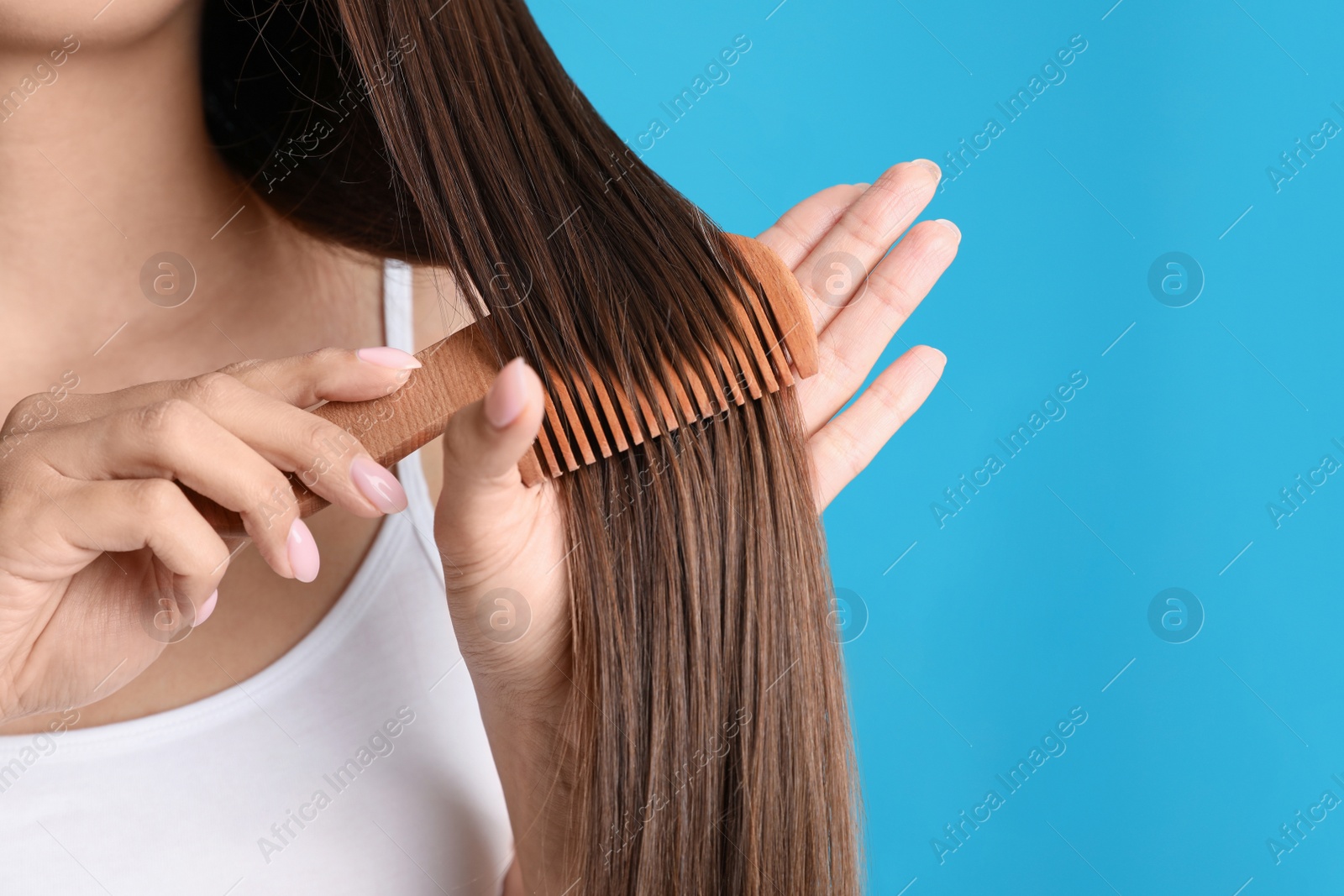 Photo of Young woman with wooden hair comb on color background, closeup. Space for text