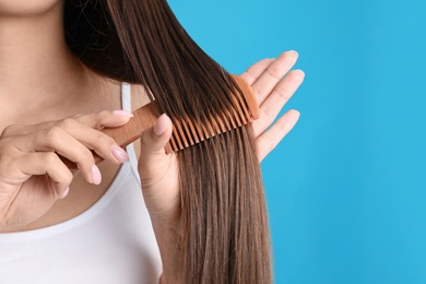 Young woman with wooden hair comb on color background, closeup. Space for text