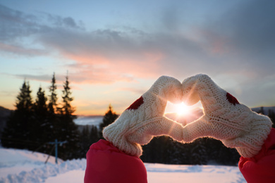 Woman making heart with hands outdoors on sunset, closeup. Winter vacation