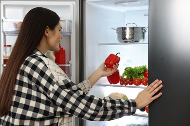 Young woman taking red bell pepper out of refrigerator