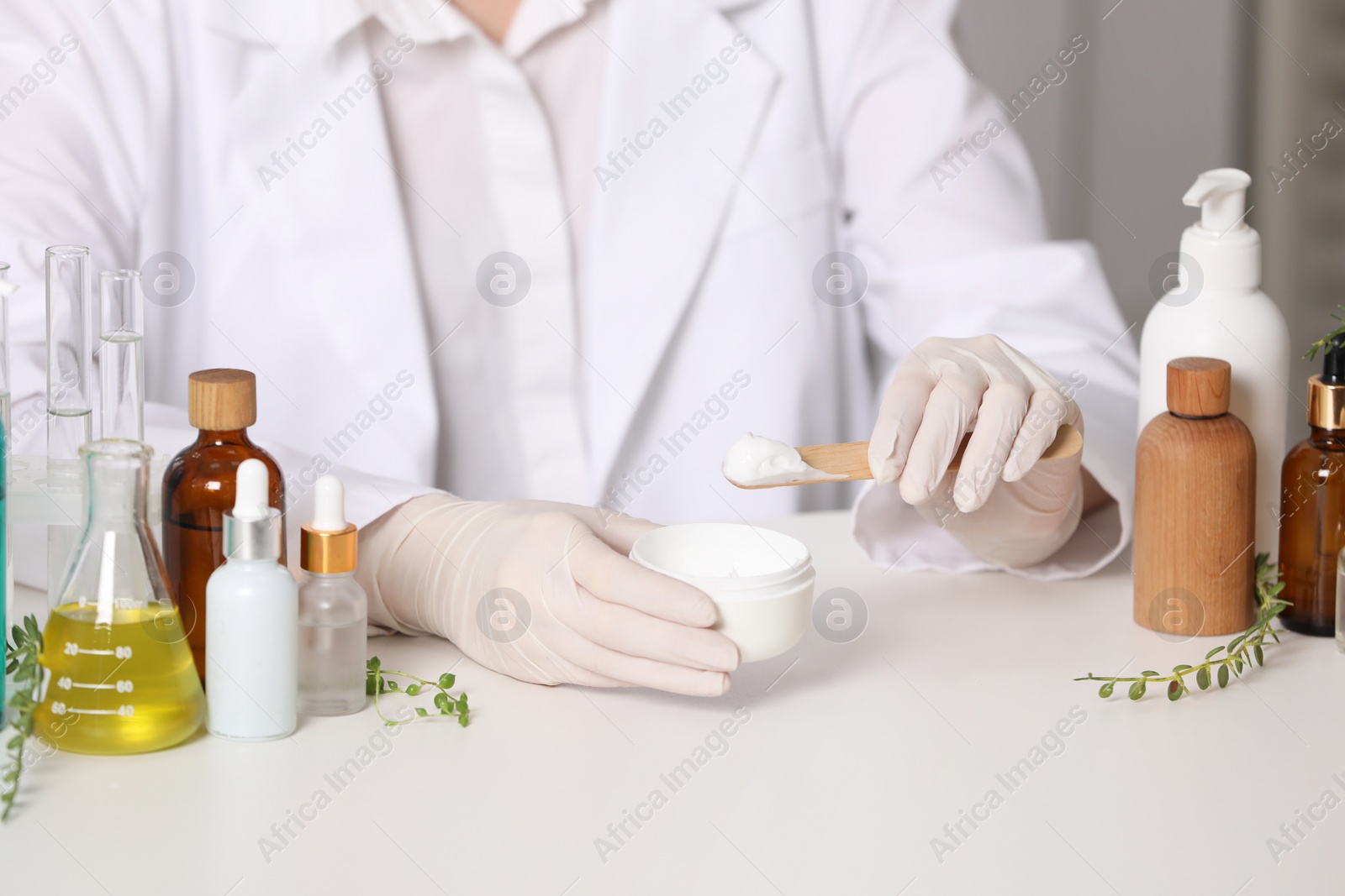 Photo of Dermatologist with jar testing cosmetic product at white table indoors, closeup