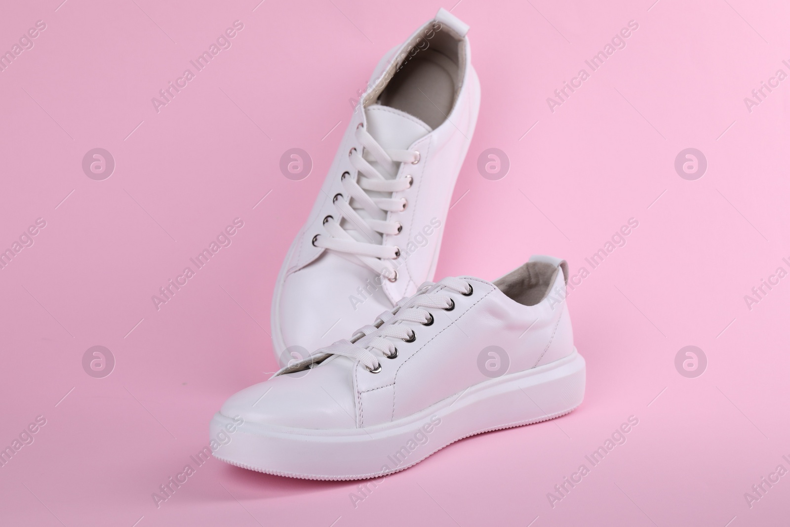 Photo of Pair of stylish white sneakers on pink background