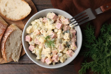 Tasty Olivier salad with boiled sausage in bowl served on wooden table, flat lay
