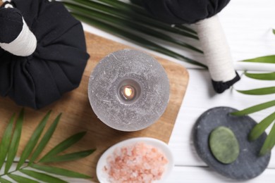 Photo of Beautiful spa composition with herbal massage bags, burning candle and leaves on white wooden table, flat lay