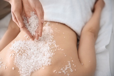 Beautiful young woman having massage with body scrub in spa salon