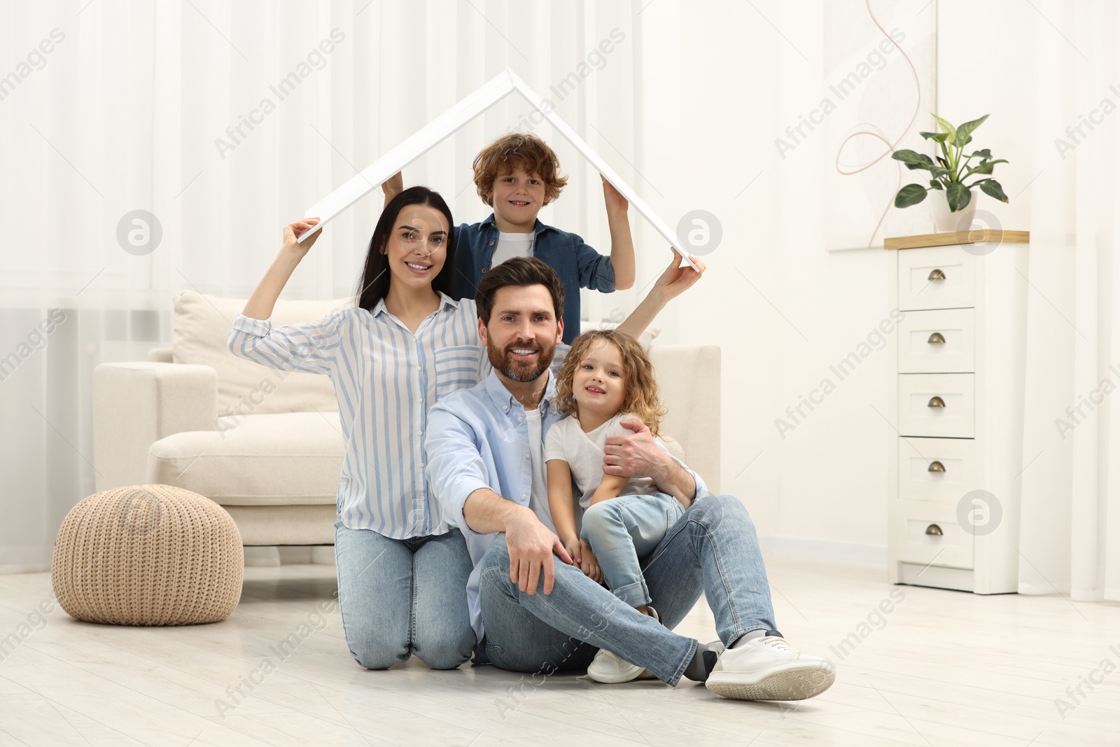 Photo of Housing concept. Happy family holding plastic roof on floor at home