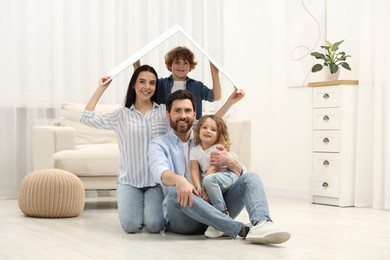 Photo of Housing concept. Happy family holding plastic roof on floor at home